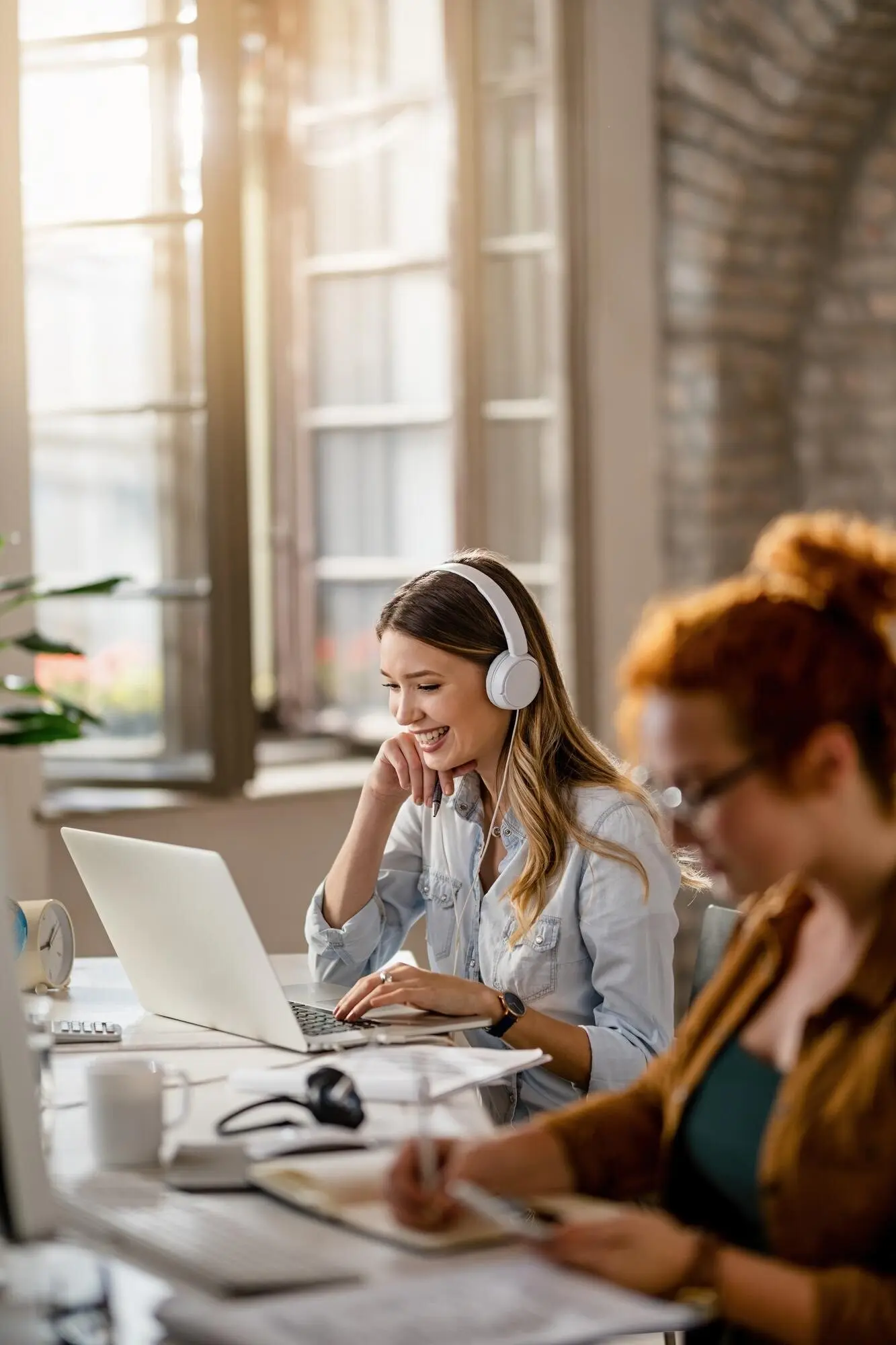 A happy female freelancer is working on a computer in the office while listening to music through headphones.