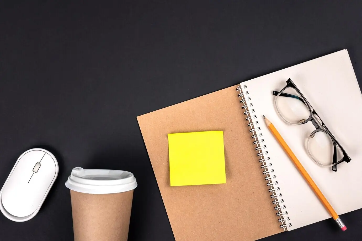 Overhead view of a workspace with a notepad, a disposable cup, a mouse, and a paper sticker.